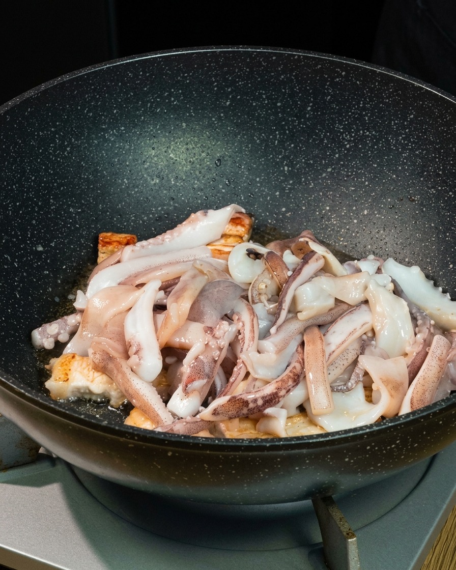 Morceaux de calamar frais disposés sur les morceaux de poitrine de porc grillés dans un grand wok noir.