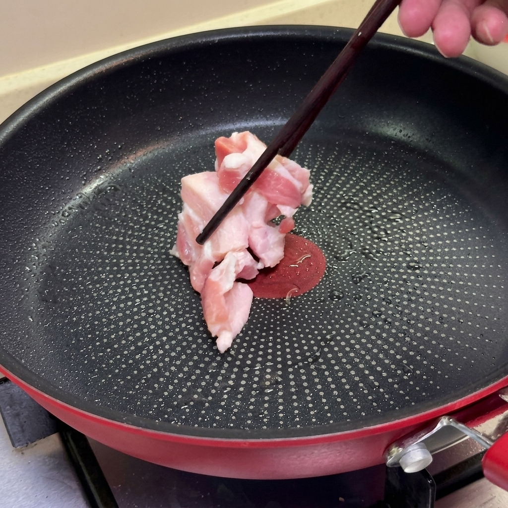 Des baguettes déposant des tranches de poitrine de porc crue dans une poêle antiadhésive chaude.