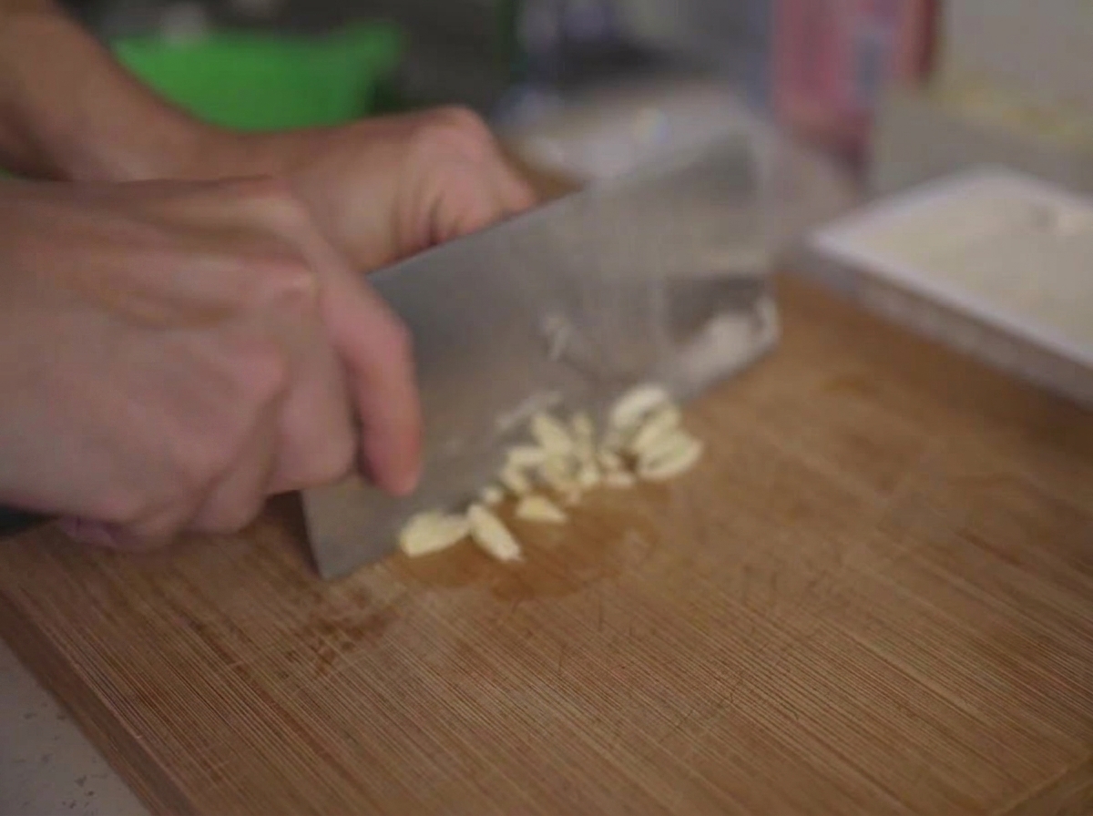 Gousses dail finement hachées sur une planche à découper en bois à laide dun couteau de cuisine.