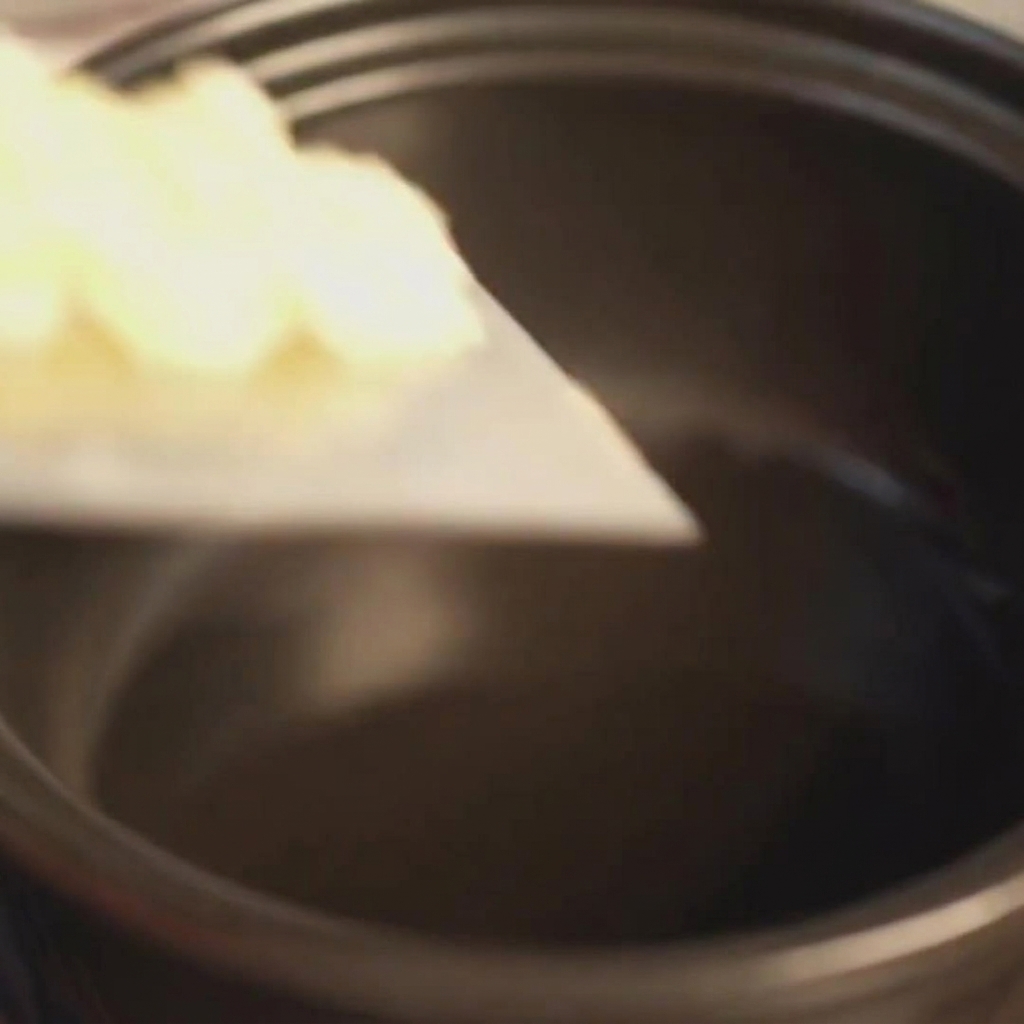 Ail finement haché ajouté dans une marmite en terre cuite noire préchauffée contenant de lhuile frémissante.