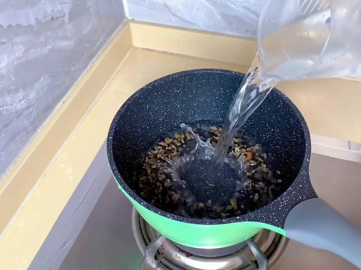 De leau claire est versée dun verre doseur en plastique dans une marmite verte sur une gazinière.