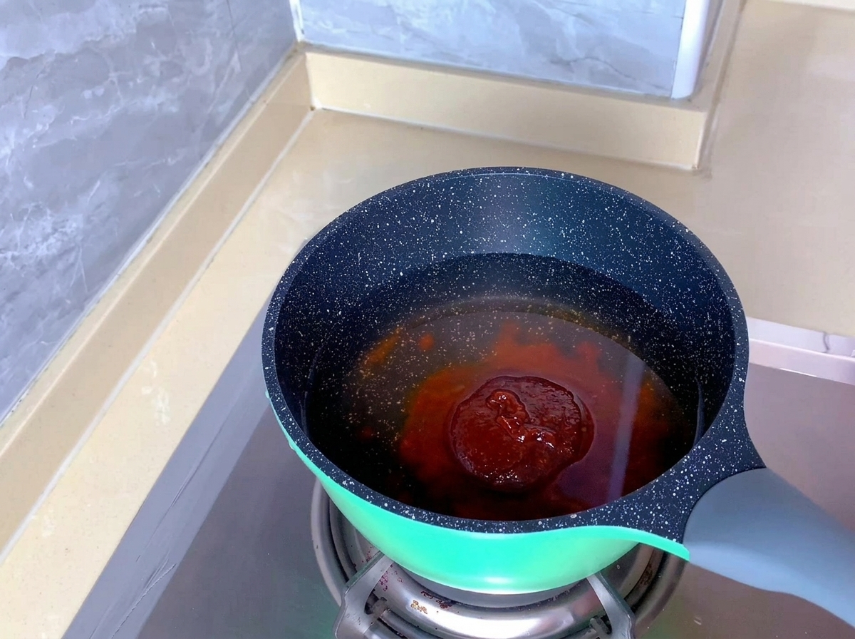 Une pâte dassaisonnement rougeâtre pour kimchi plongée dans leau claire dune marmite mouchetée.