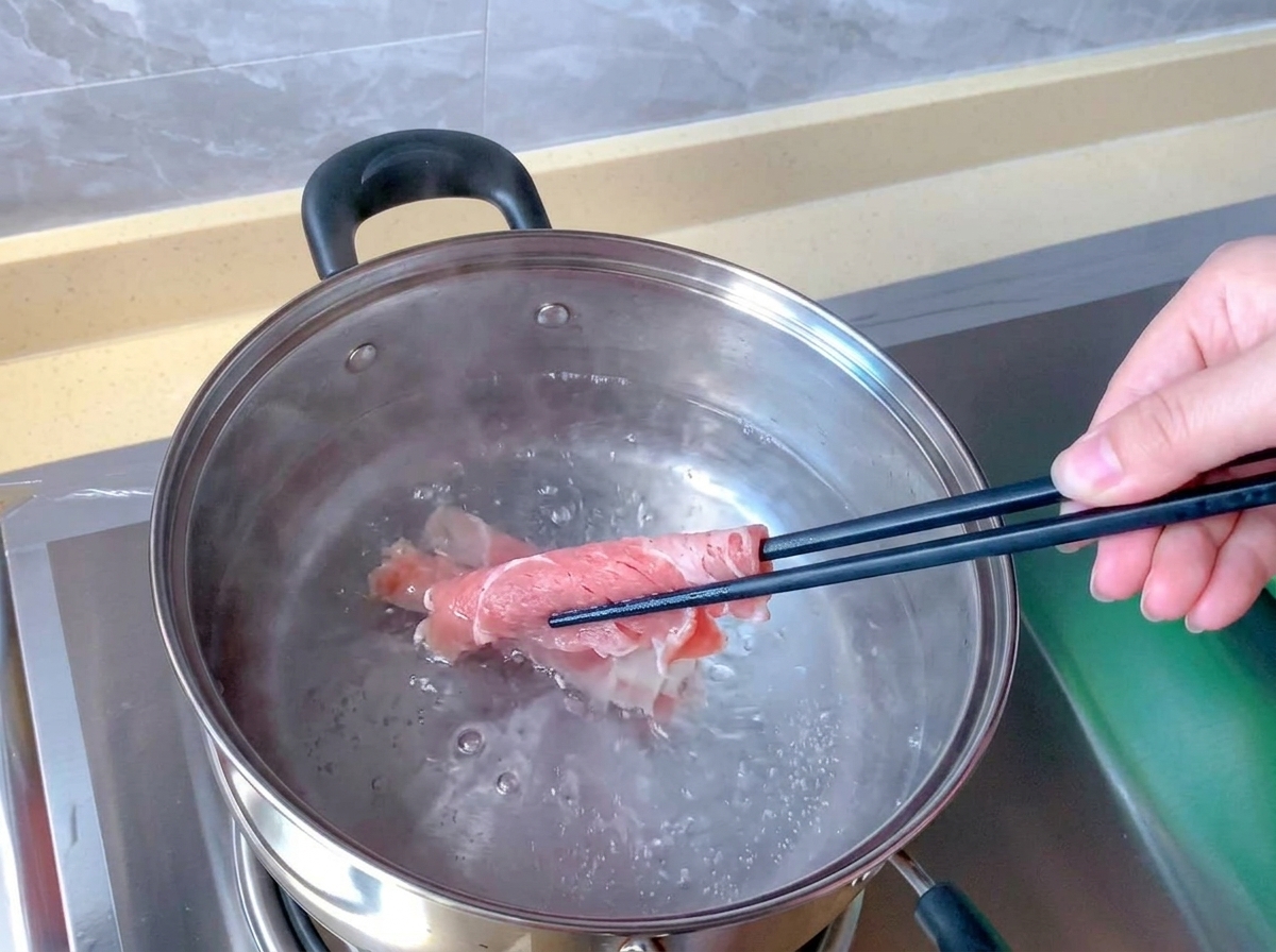 Des baguettes plongent un roulé de bœuf cru et rosé dans une casserole en inox remplie deau bouillante.