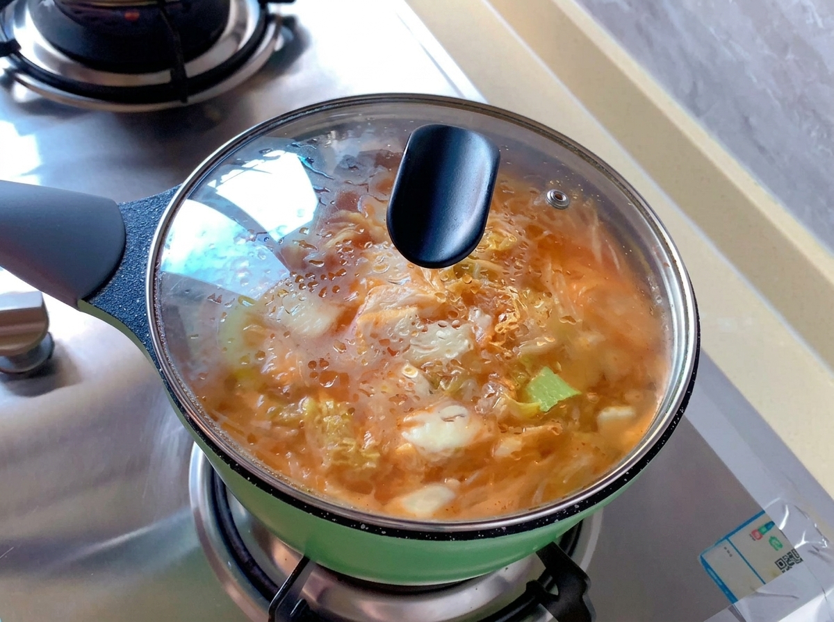 Une petite marmite verte remplie de soupe au kimchi couverte par un couvercle en verre transparent avec de la condensation.