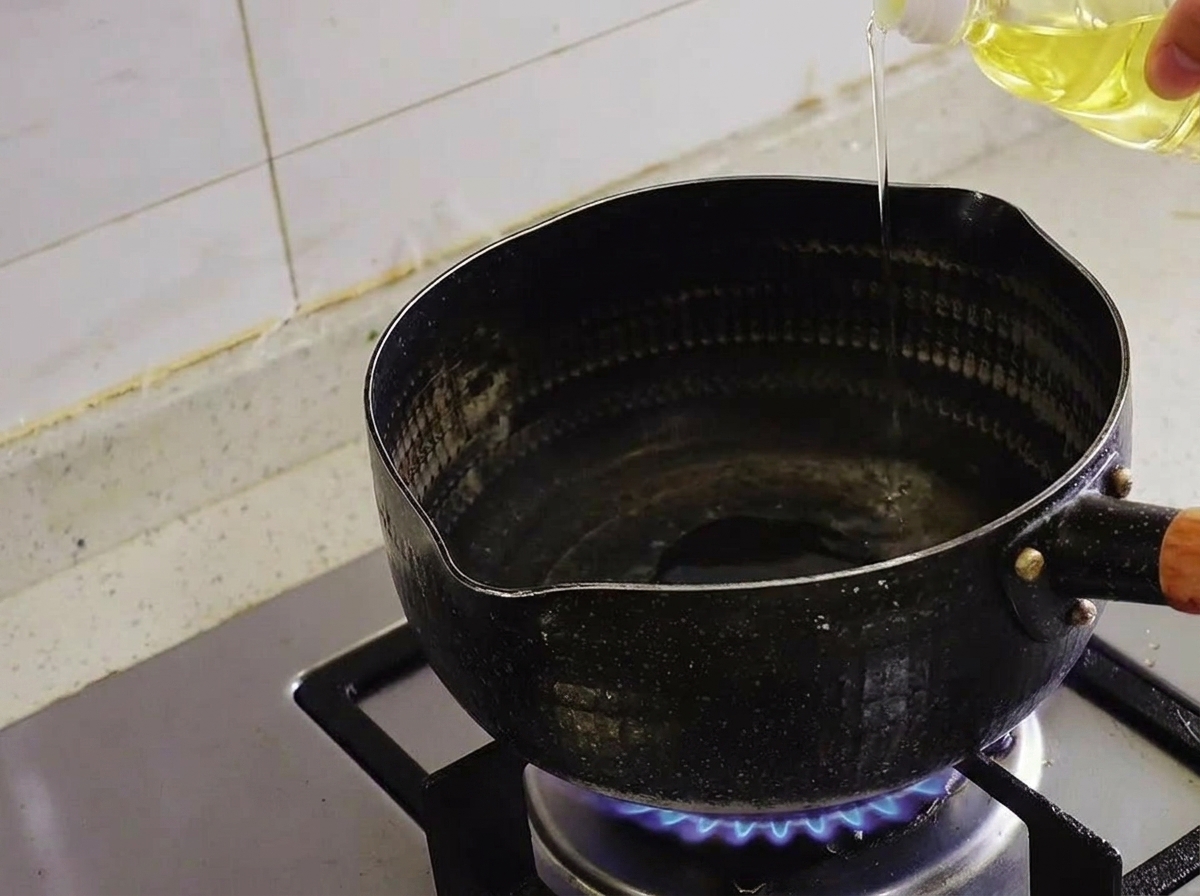 De lhuile claire versée dune bouteille dans une casserole noire sur un brûleur de cuisinière à gaz allumé.