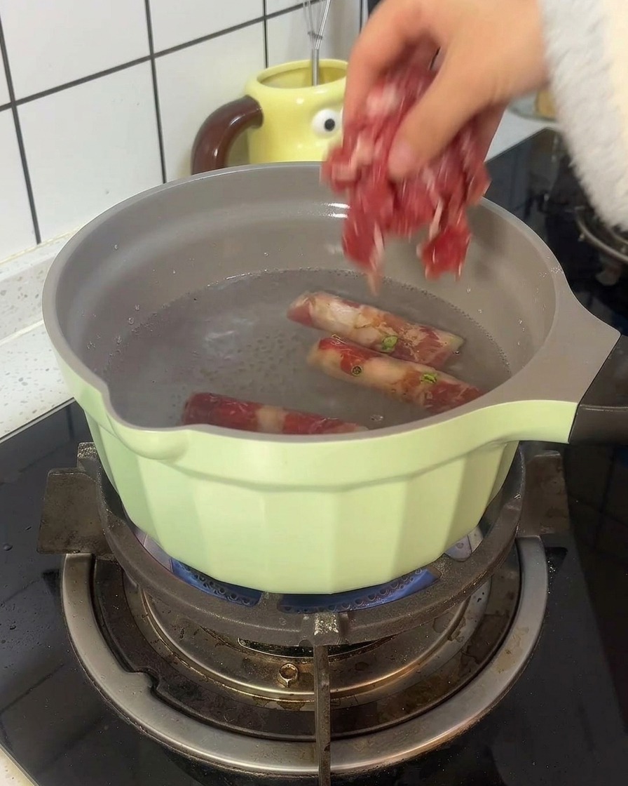 Des rouleaux de bœuf blanchissent dans une casserole vert clair remplie deau bouillante.