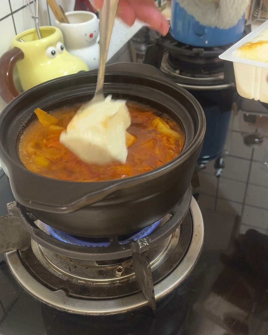 Une cuillère prélève de gros morceaux de tofu soyeux pour les plonger dans un bouillon rouge bouillonnant dans un pot en terre cuite.