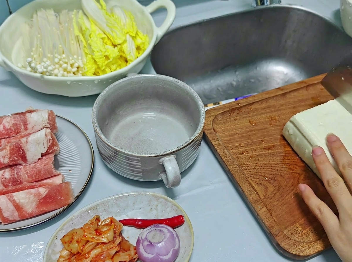 Gros plan sur une main utilisant un couteau de cuisine pour trancher un gros bloc de tofu blanc en morceaux rectangulaires épais sur une planche à découper en bois.