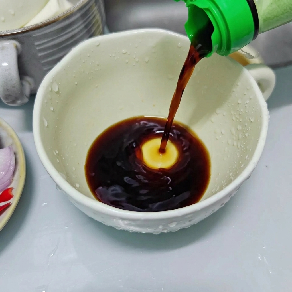 De la sauce soja foncée versée dune bouteille à bouchon vert dans une tasse en céramique blanche pour préparer la sauce dassaisonnement.