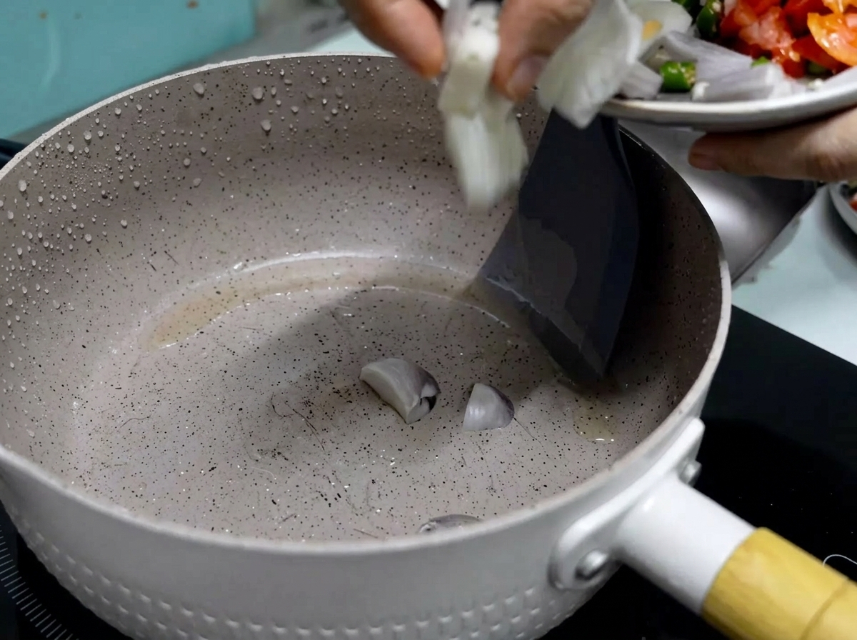 Une main faisant glisser des oignons rouges fraîchement coupés dune petite assiette dans une poêle antiadhésive chauffée avec de lhuile frémissante.