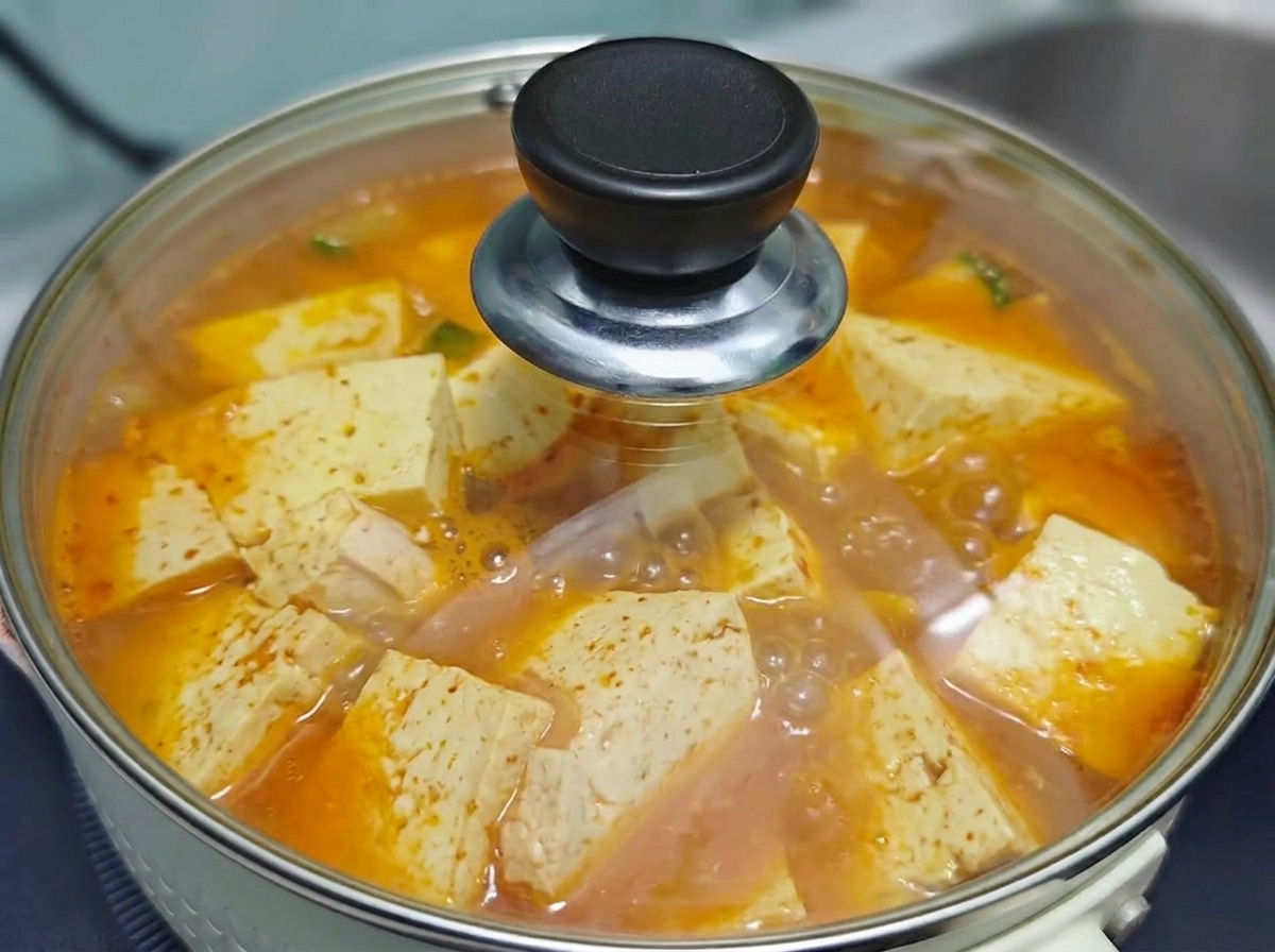 Un couvercle en verre transparent recouvrant la marmite bouillonnante de soupe coréenne au kimchi, bœuf et tofu pendant quelle mijote sur la cuisinière.