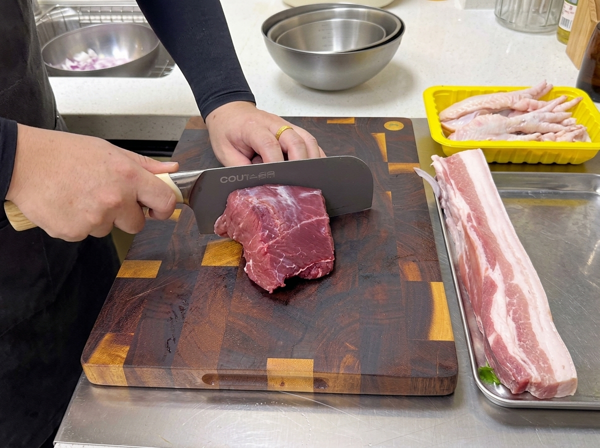 Un chef utilisant un grand couteau professionnel pour couper un morceau de basse côte de bœuf crue sur une planche en bois.