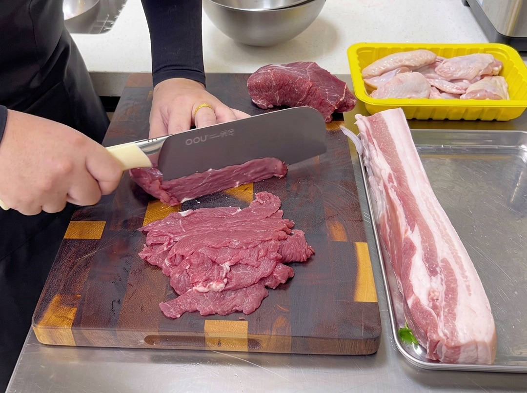Découpe de fines tranches de bœuf cru dans le sens inverse des fibres sur une planche en bois avec un couteau de chef.