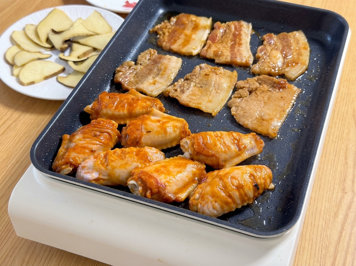 Des tranches de poitrine de porc marinée et des ailes de poulet orange dOrléans grésillant ensemble sur une plancha électrique chaude.