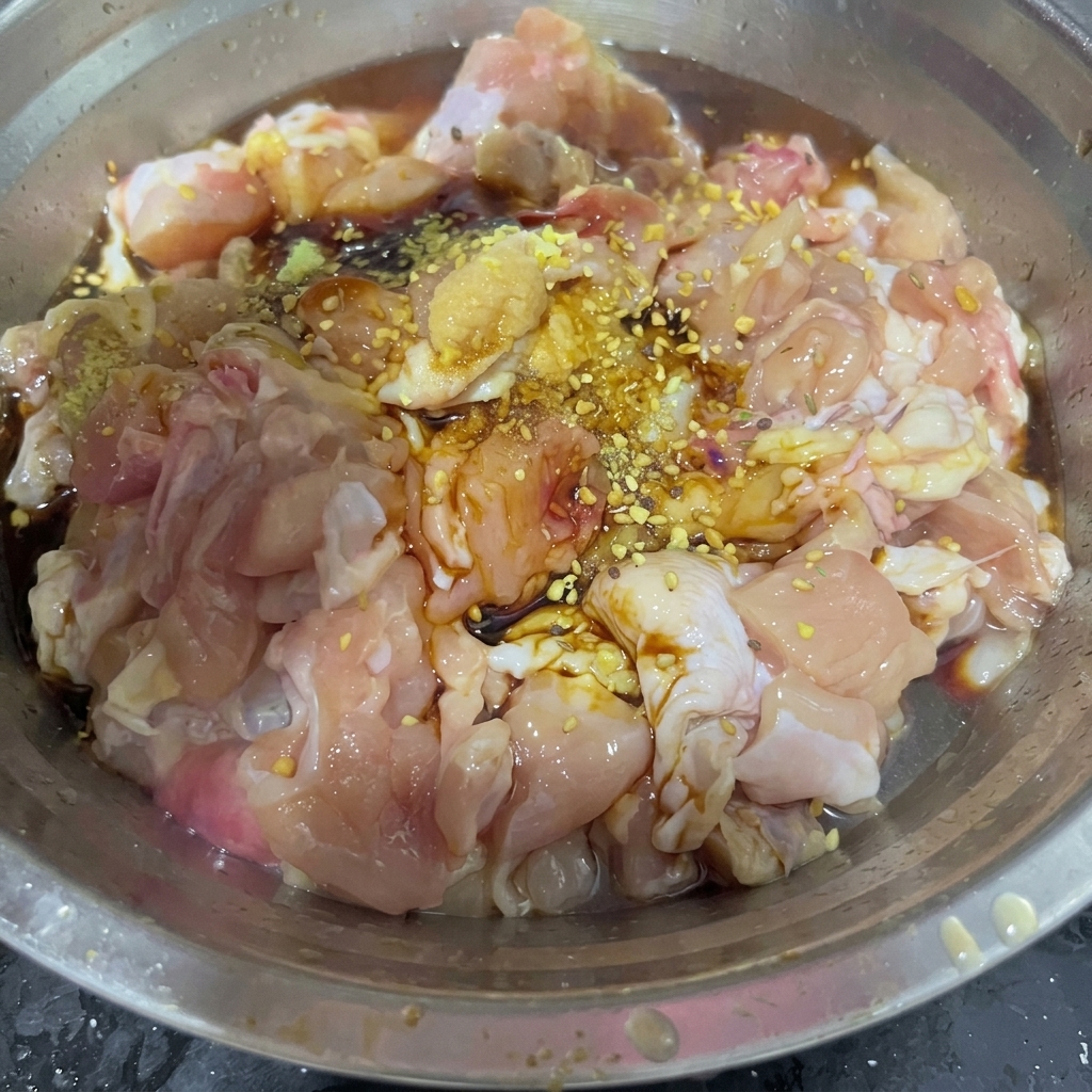 Une cuillerée dépices sèches pour barbecue parsemée sur des morceaux de poulet marinés à lintérieur dun bol à mélanger en acier inoxydable.