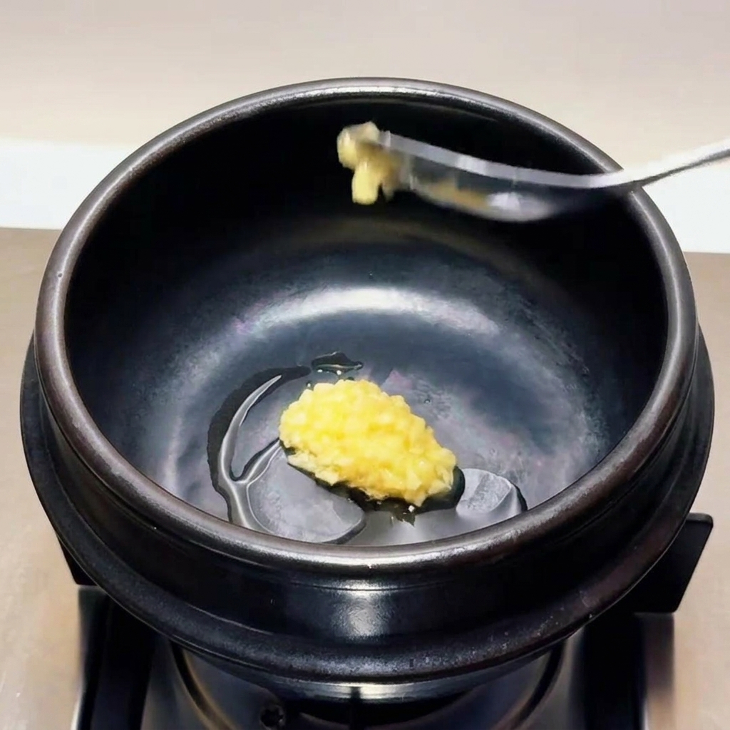 Une cuillère dail finement émincé déposée dans lhuile chaude à lintérieur dun pot de cuisson en pierre noire.