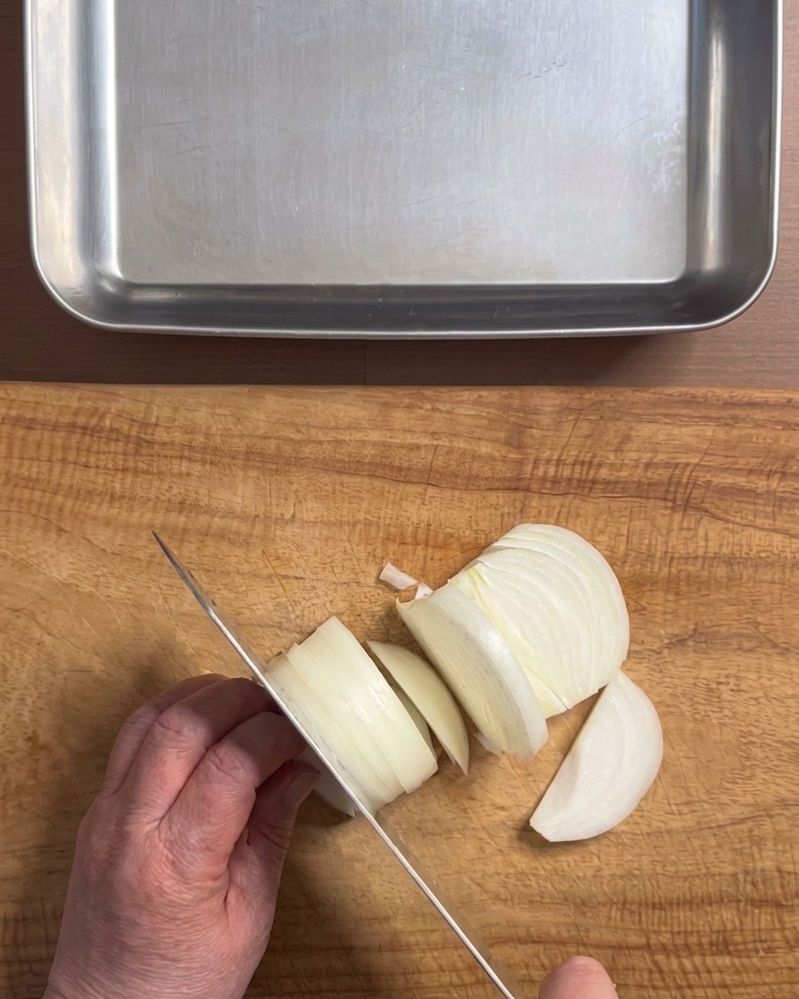 Mains utilisant un couteau pour couper un oignon blanc en tranches épaisses sur une planche à découper en bois.