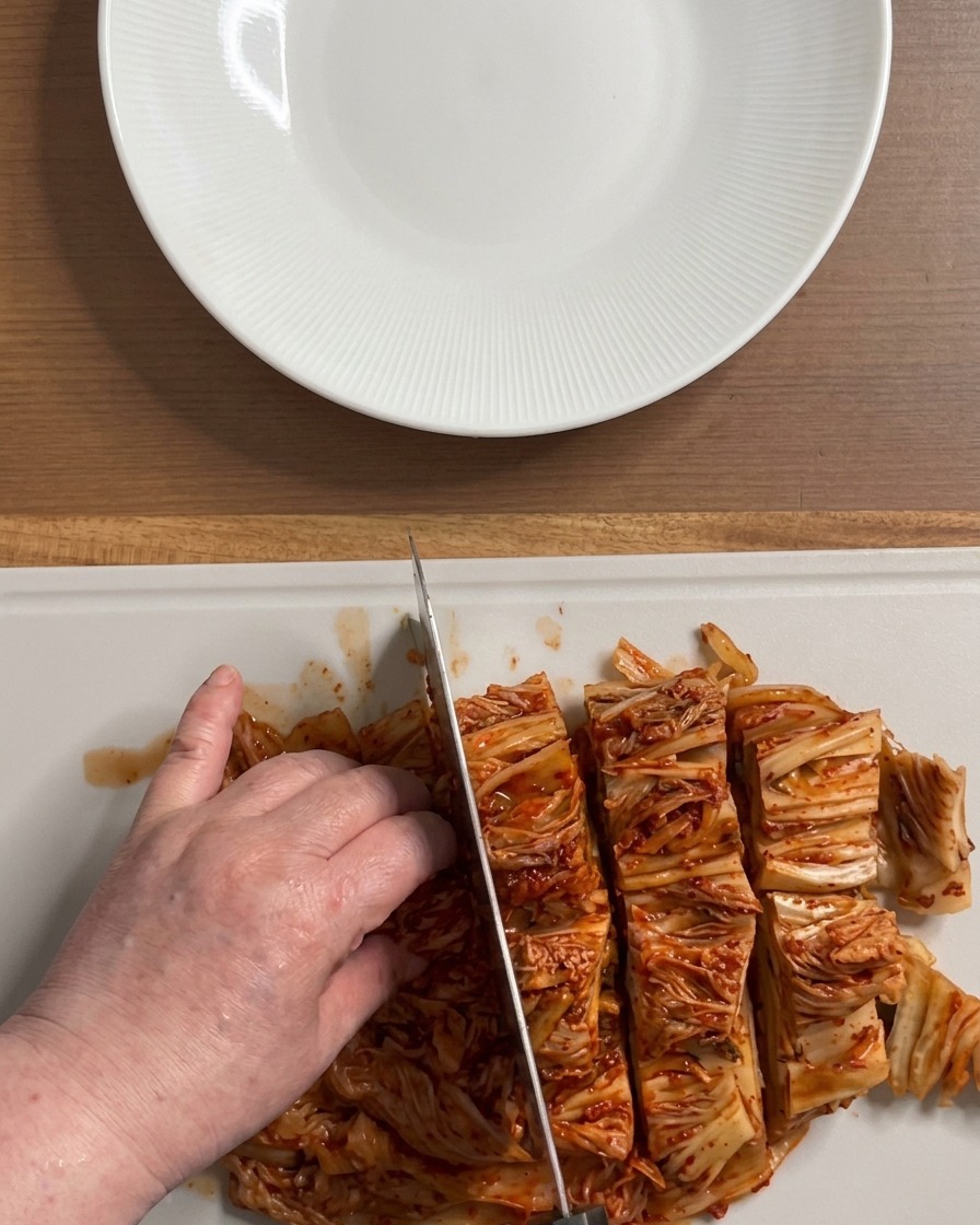 Mains coupant un gros bloc de kimchi rouge et brillant en morceaux de la taille dune bouchée sur une planche blanche.
