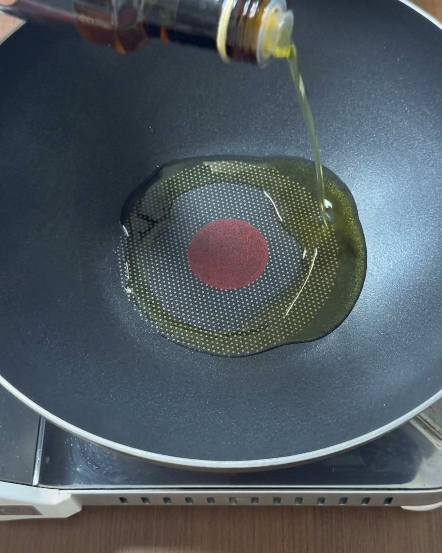 Huile dorée versée depuis une bouteille en verre au centre dun wok noir bien chaud.
