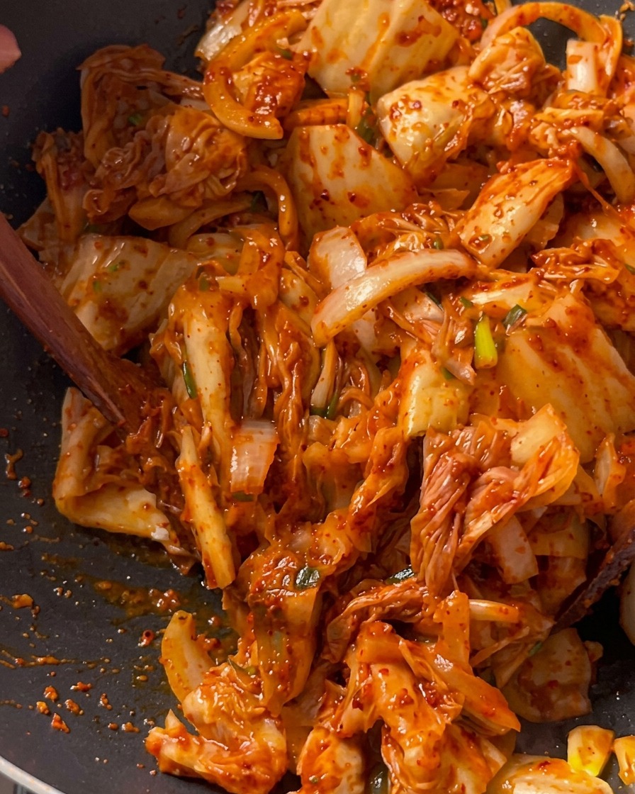 Morceaux de kimchi sautés activement avec le porc et les oignons dans un grand wok noir à laide dune spatule en bois.