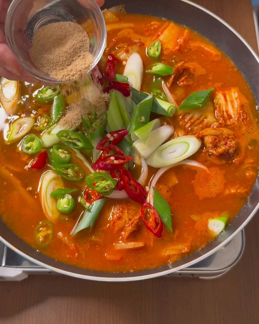 Poudre de bouillon de bœuf Dashida saupoudrée depuis une coupelle en verre sur la surface dun ragoût rouge garni daromates.