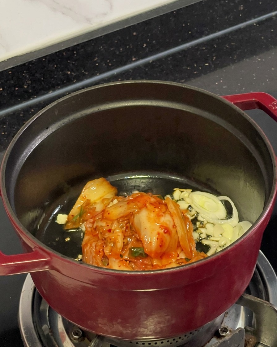Kimchi rouge haché, ail émincé et oignons verts cuisant dans lhuile à lintérieur dune marmite.