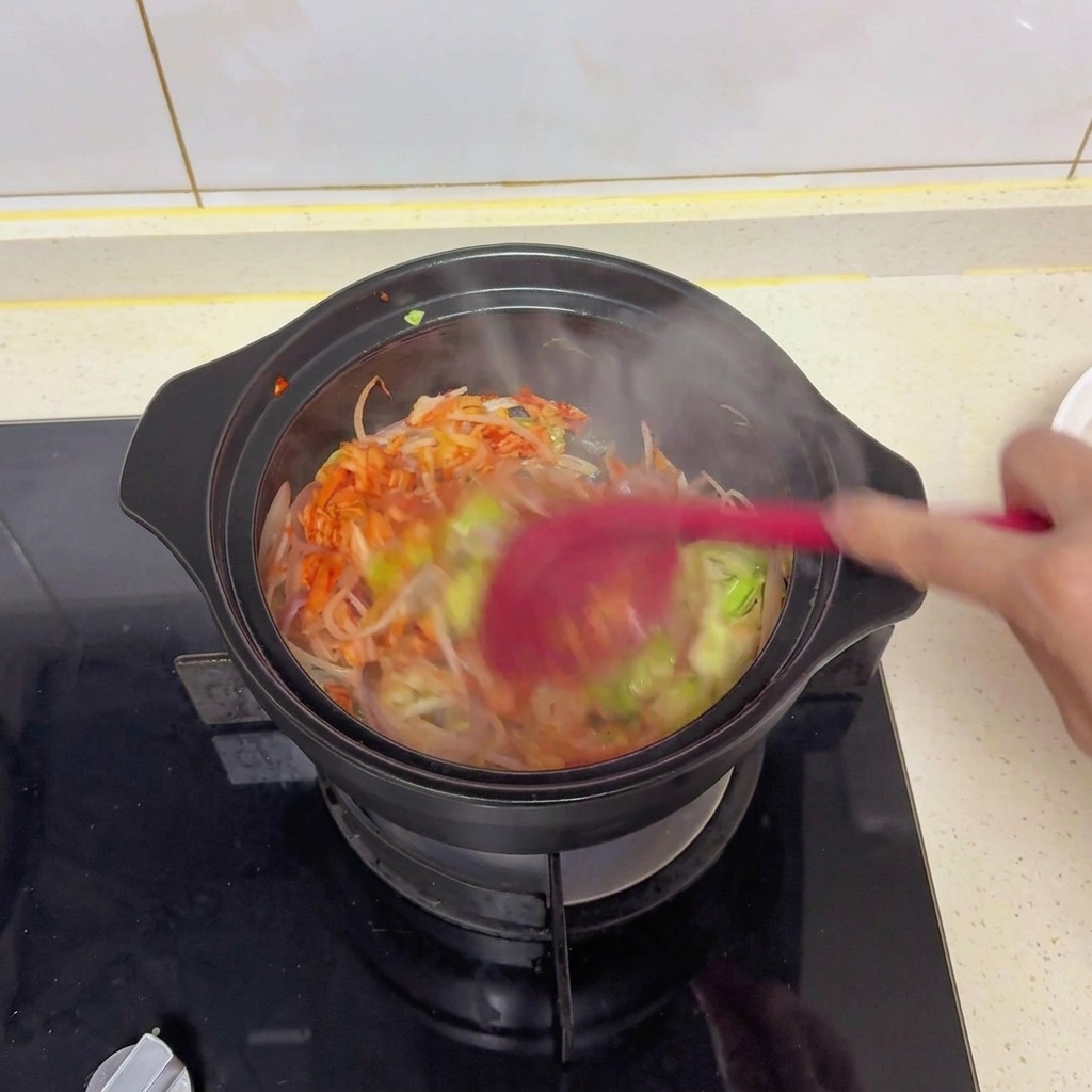 Légumes mélangés et kimchi sautés dans une marmite noire avec une spatule rouge pour incorporer le sel, la sauce soja et les condiments.