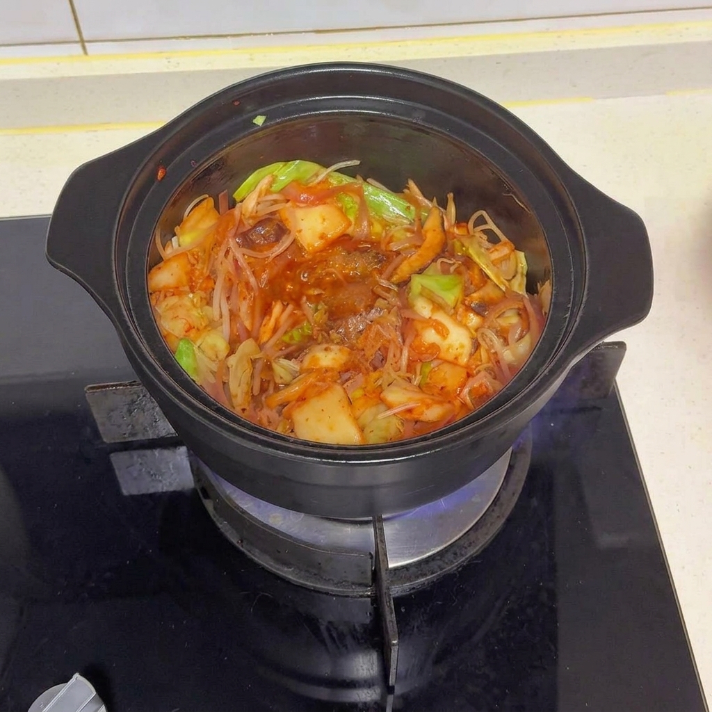 Une marmite noire remplie de légumes et de kimchi sautés, garnie de divers assaisonnements et de piment rouge en poudre.