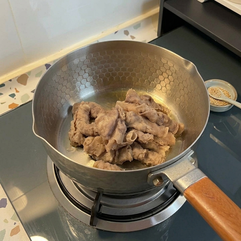 Du bœuf finement émincé saisi dans une marmite en acier inoxydable sur une cuisinière à gaz.