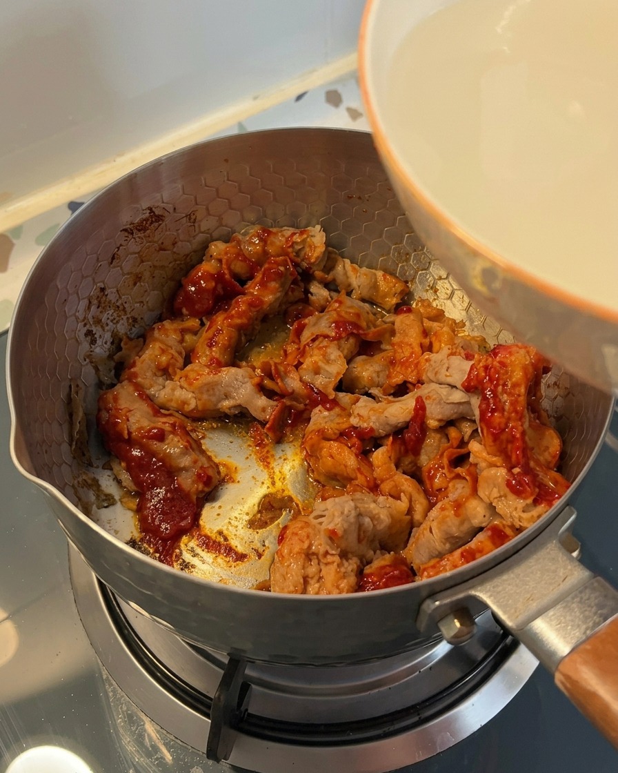 De leau de rinçage du riz trouble versée depuis un bol blanc dans une marmite contenant le bœuf assaisonné.