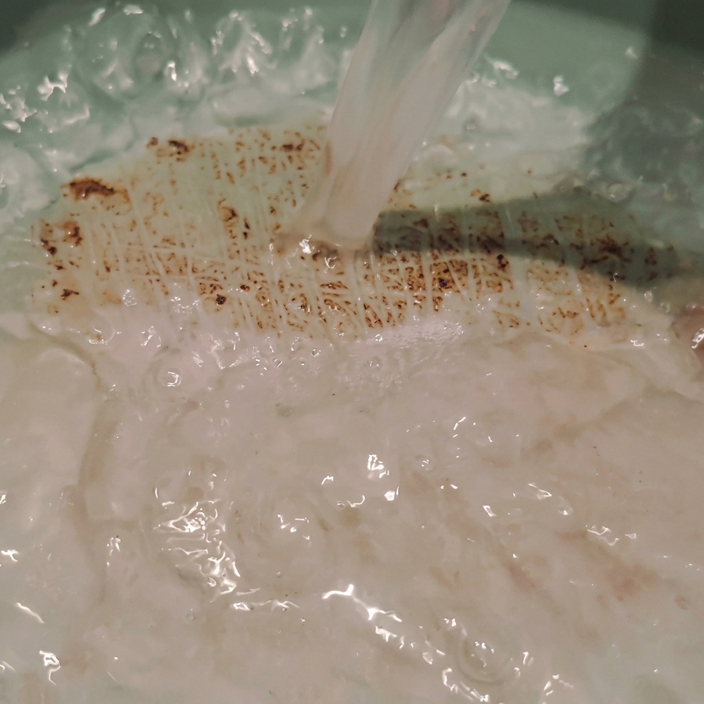 De leau de riz trouble versée directement dans une marmite, créant de légers remous et des bulles.