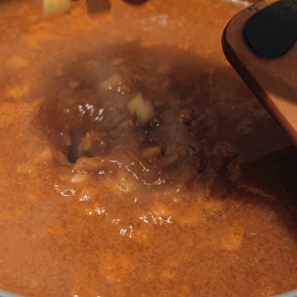 Dés de pommes de terre crues jetés dans un bouillon orange frémissant doù séchappe de la vapeur.
