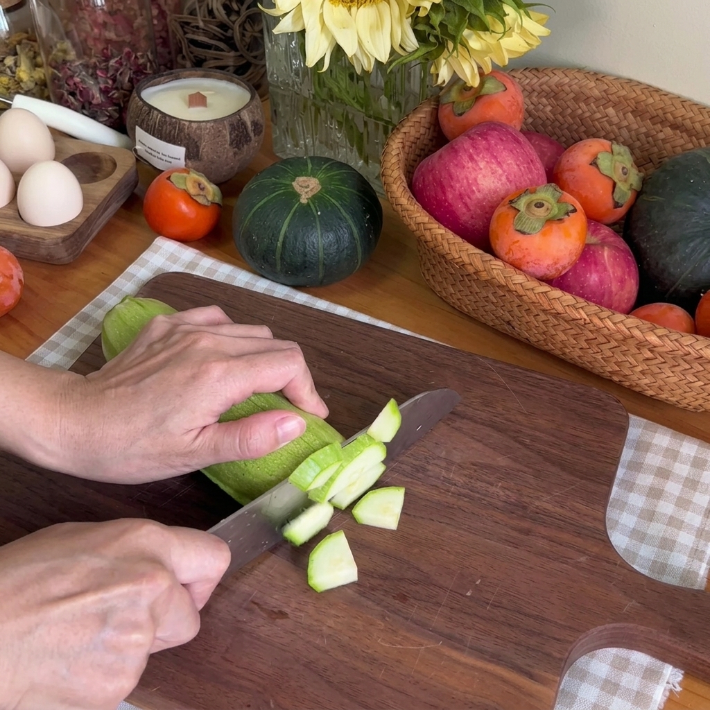 Gros plan sur des mains utilisant un couteau de chef pour couper une courgette verte en petits morceaux sur une planche en bois.