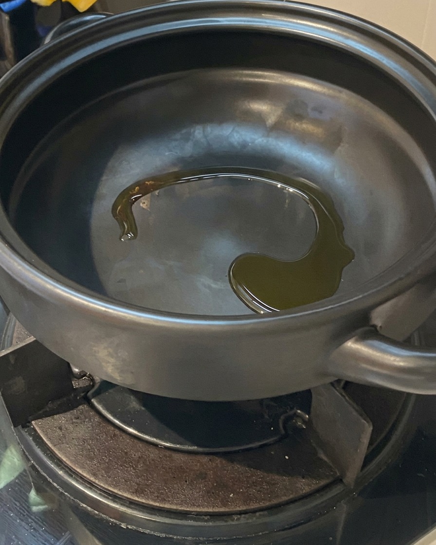 Huile de cuisson brillante au fond dune marmite en terre cuite noire chauffée sur un brûleur de cuisinière à gaz.