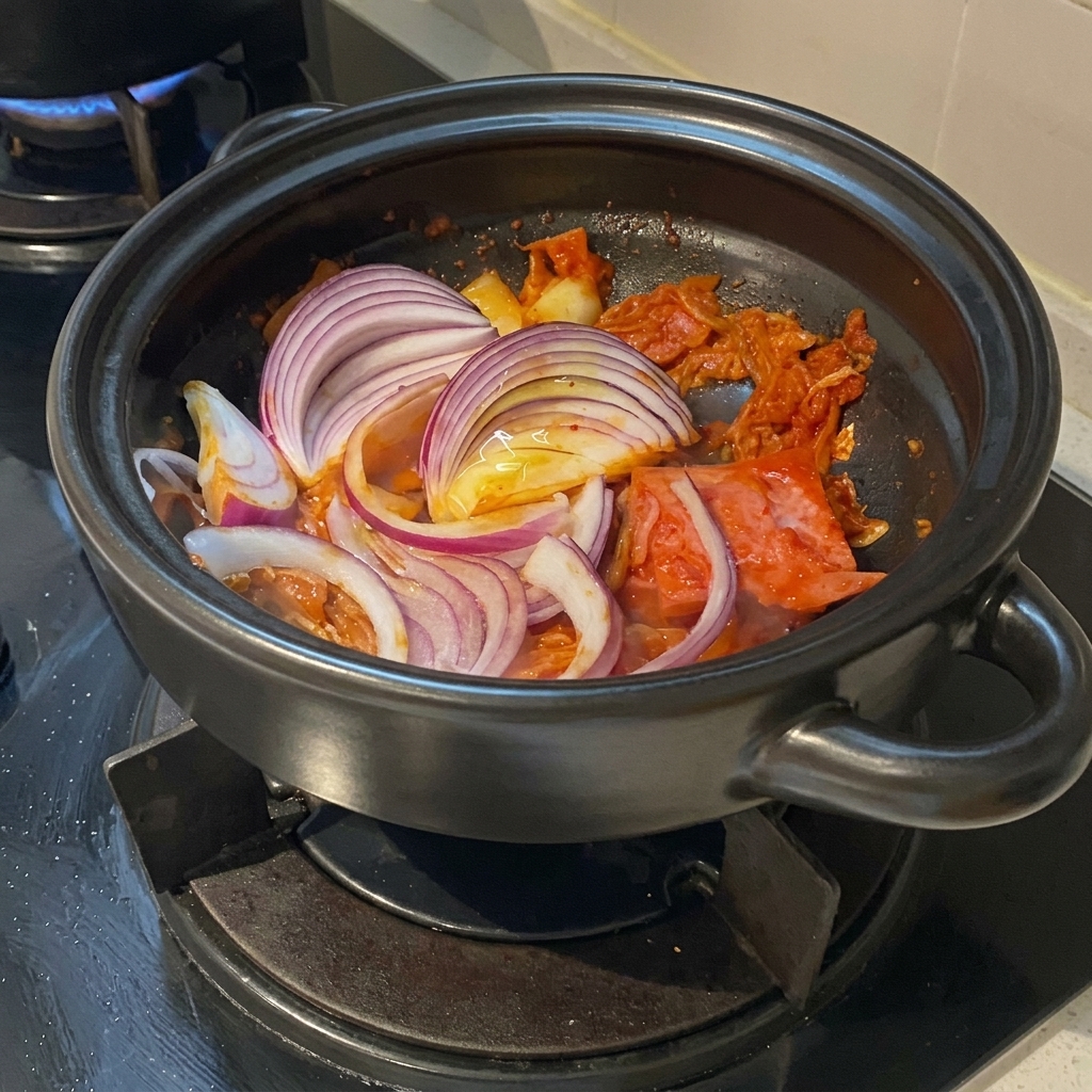 Épaisses tranches doignon rouge disposées sur un sauté de kimchi et de poitrine de porc dans une marmite en terre cuite.