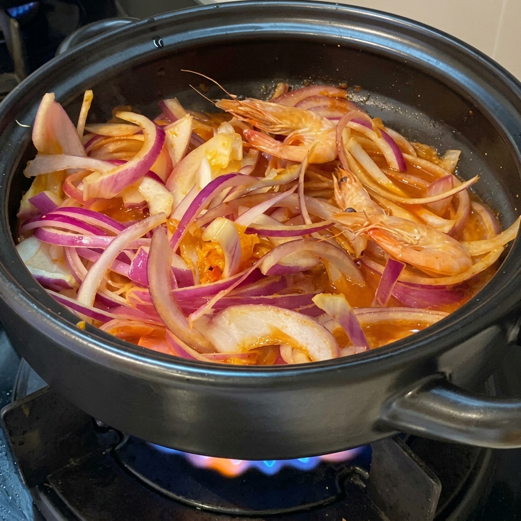 Crevettes roses fraîches entières nichées parmi les tranches doignon rouge et le kimchi dans une marmite en terre cuite noire.