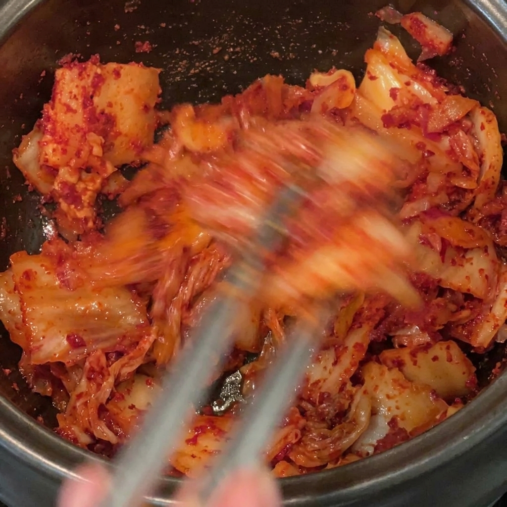 Mélange vigoureux de la poudre de piment rouge avec le kimchi et la poitrine de porc dans une marmite noire.