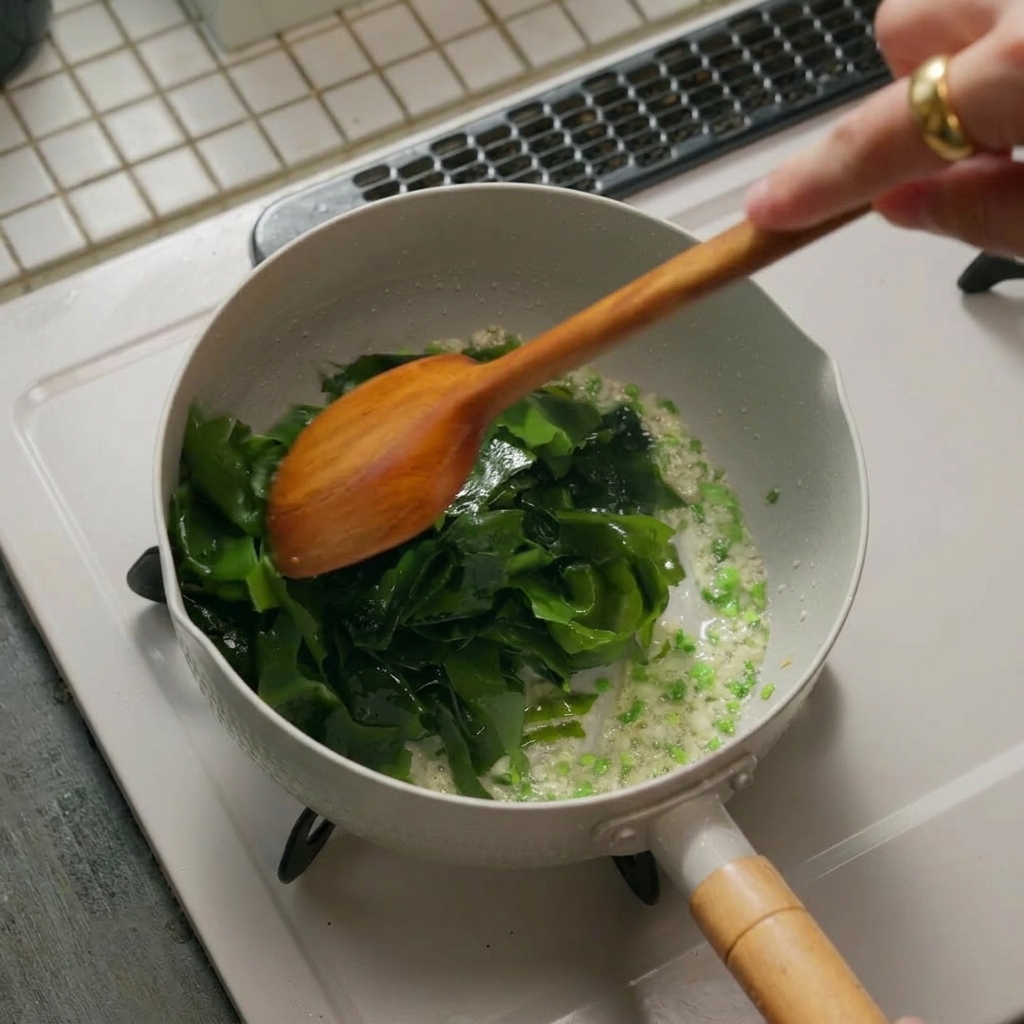 Des algues réhydratées ajoutées dans une poêle avec les aromates, mélangées avec une spatule.