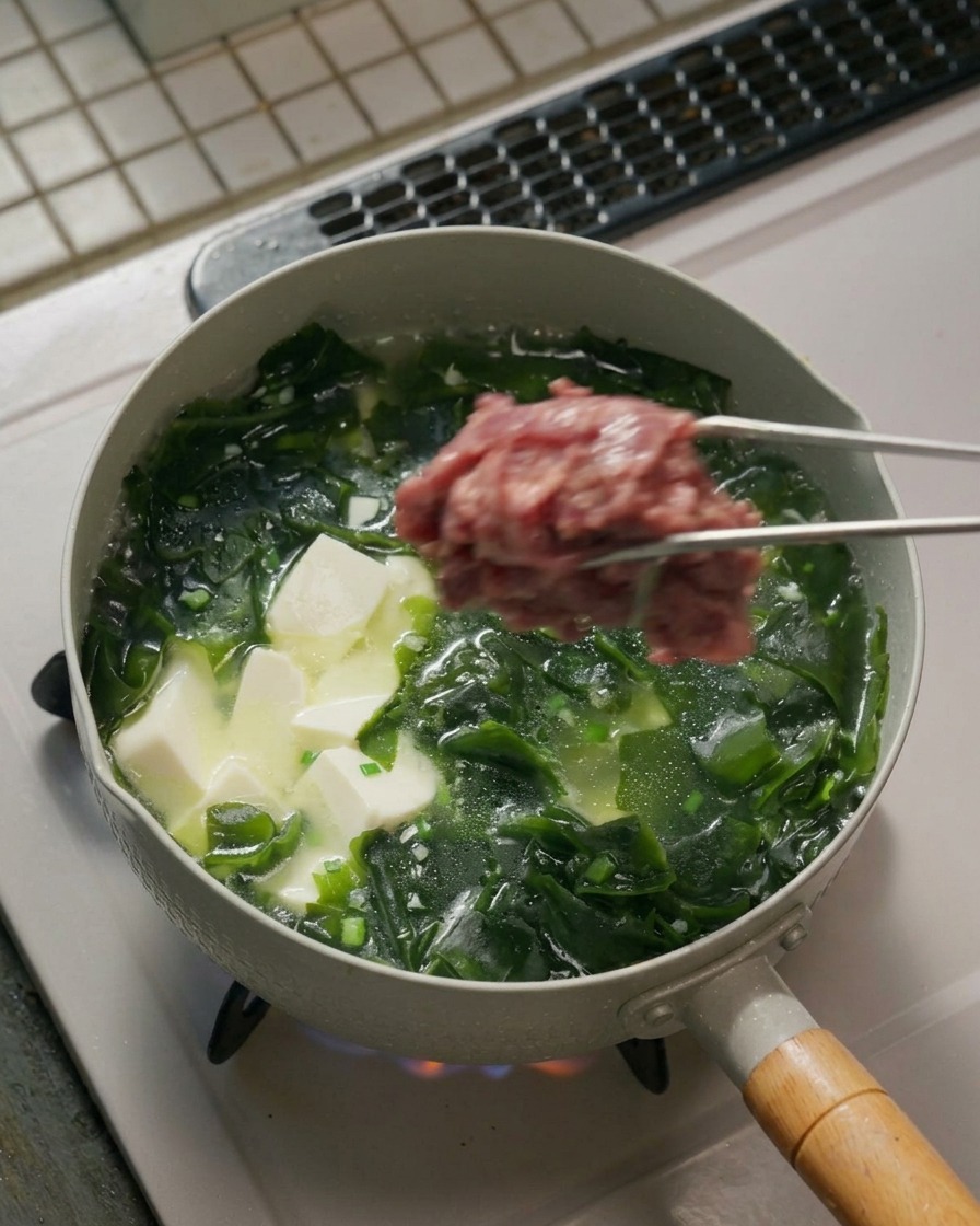 Des pinces déposant des morceaux de bœuf mariné dans une casserole bouillante.