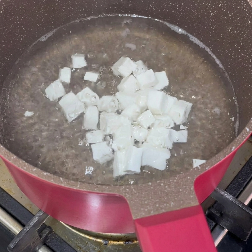 Cubes de tofu soyeux blanchissant dans une casserole deau bouillante.