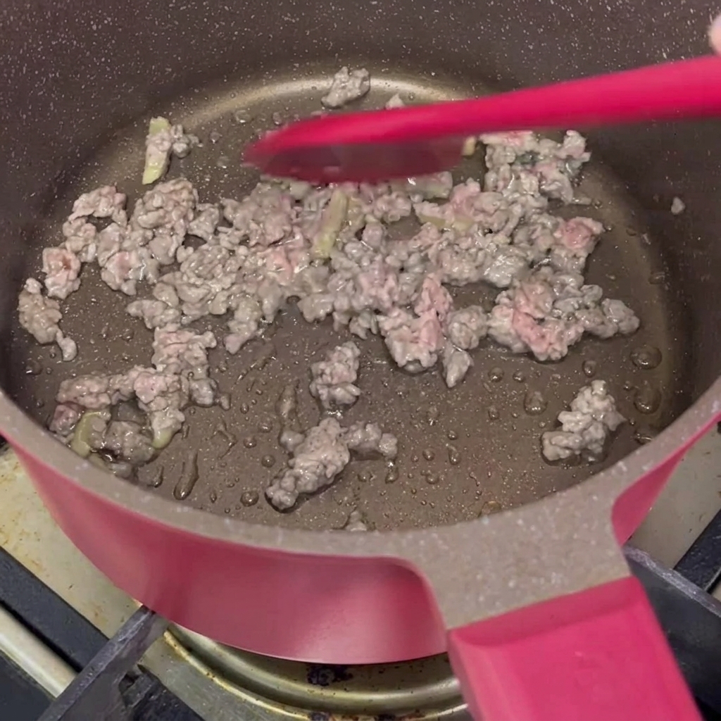 Bœuf haché mariné en train de cuire dans une poêle rose.