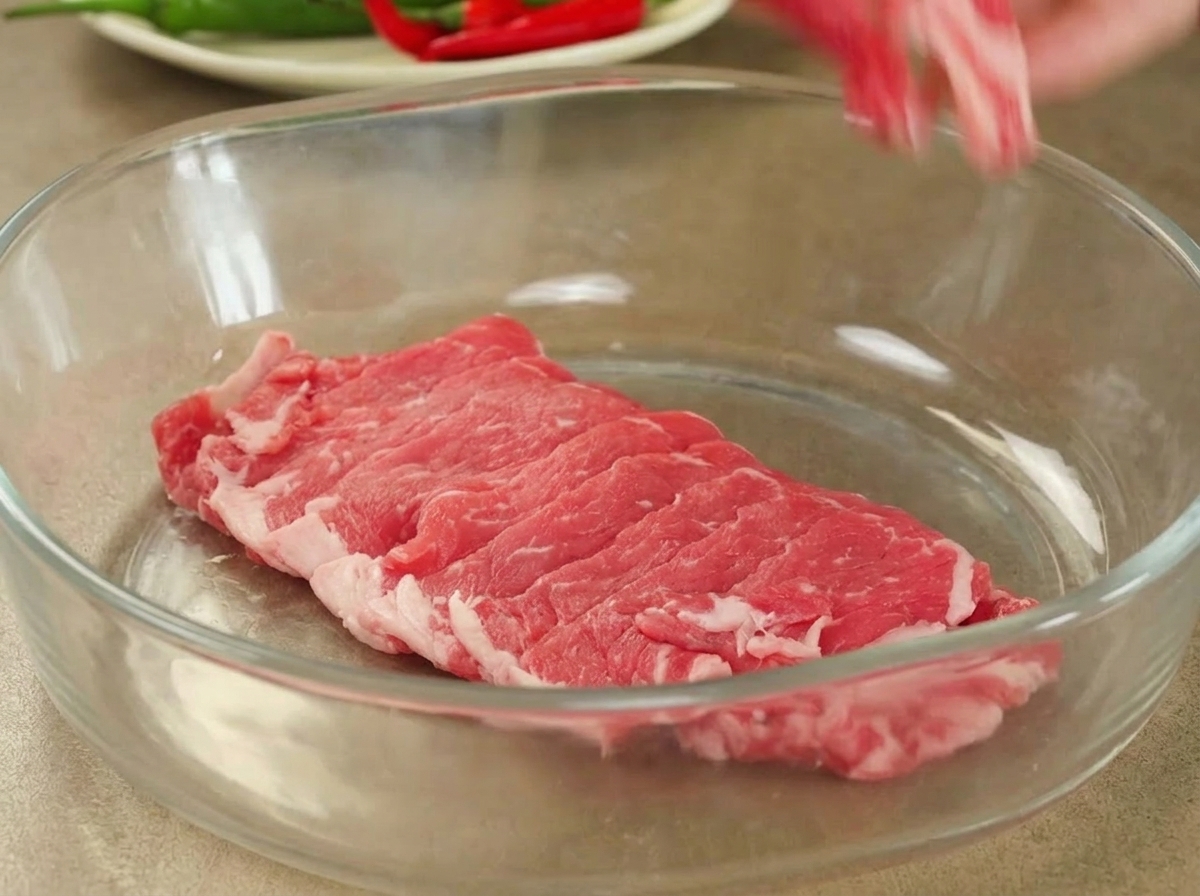 Tranches de bœuf cru fraîchement coupées disposées dans un grand bol en verre.