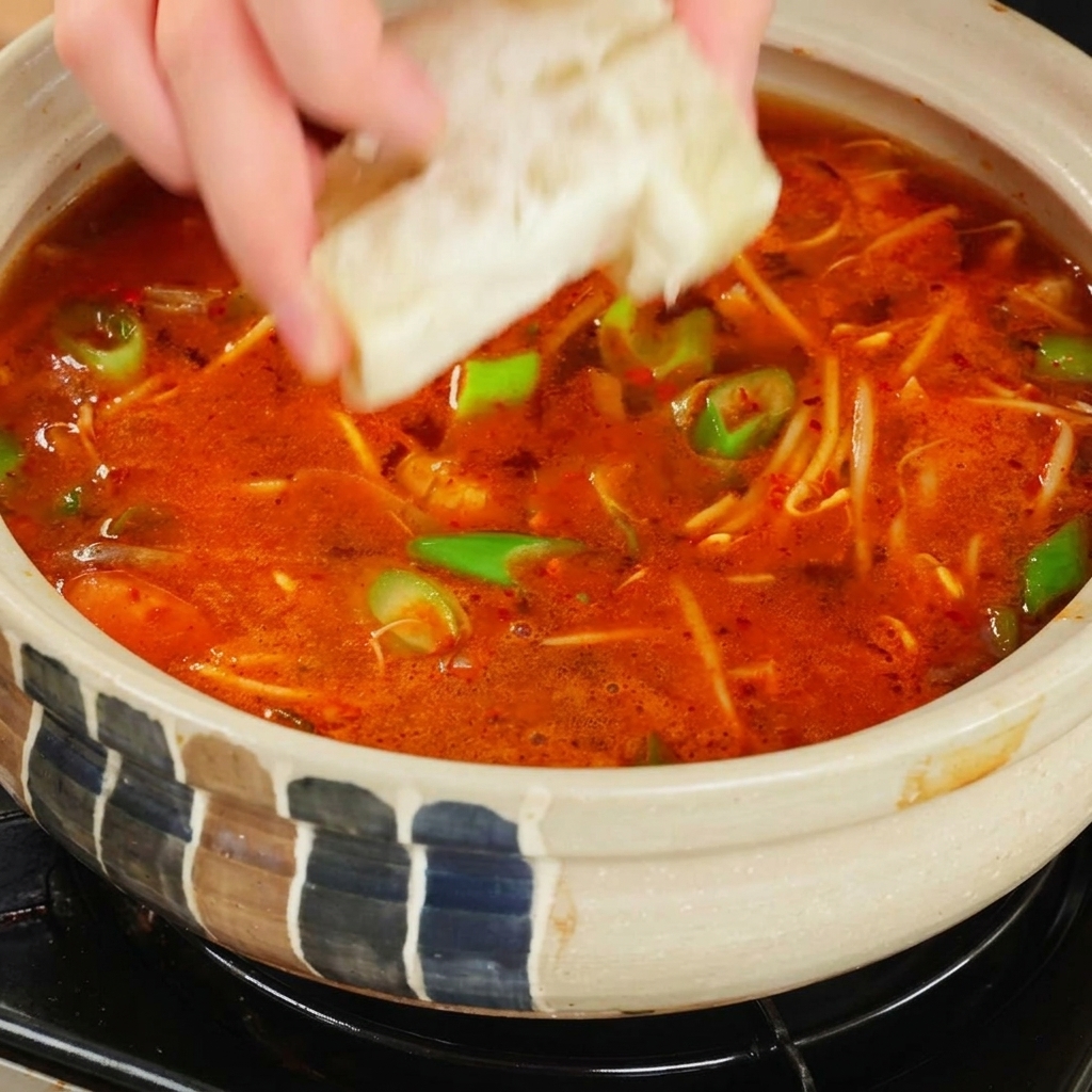 Main ajoutant un cube de bouillon dans la soupe rouge bouillonnante.