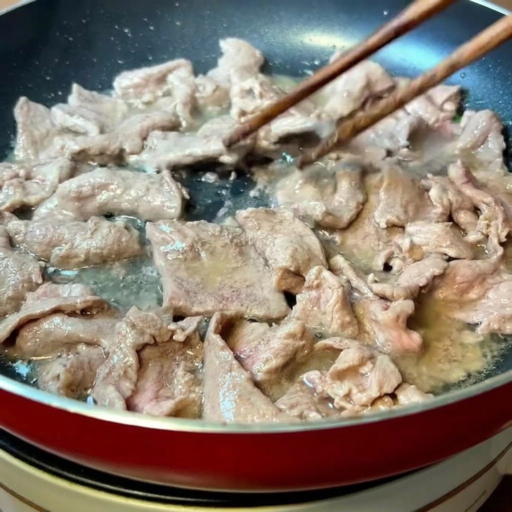 Tranches de bœuf marinées en cours de cuisson à la poêle avec des baguettes.