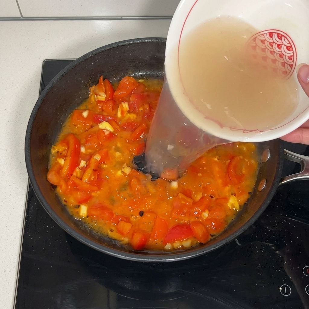 Bouillon versé sur les tomates dans la poêle.