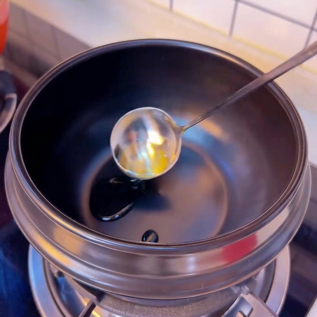 Huile de camélia versée depuis une louche argentée dans un pot en terre cuite préchauffé.
