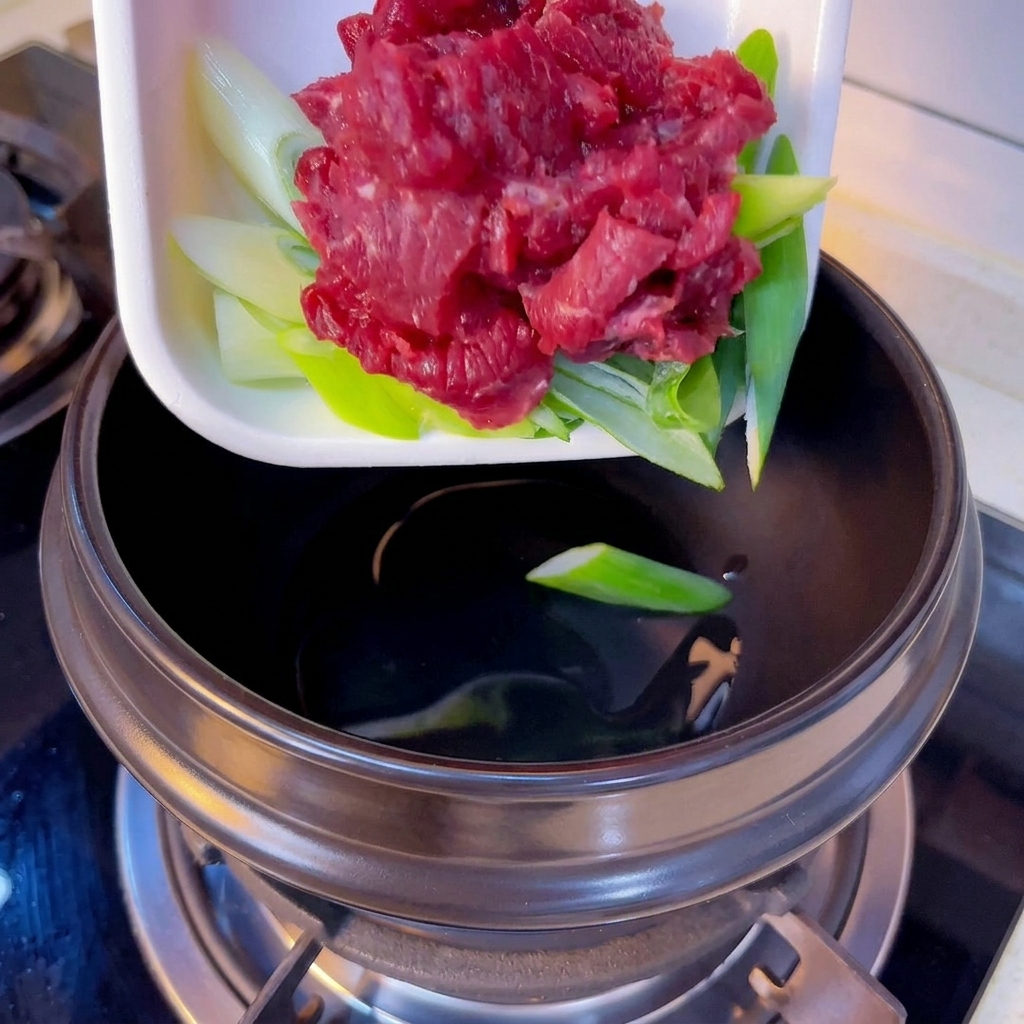Émincé de bœuf et oignons verts ajoutés dans le pot en terre cuite.