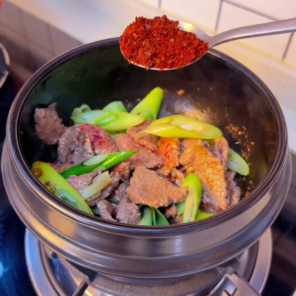 Cuillère argentée versant la poudre de piment gros dans le pot.