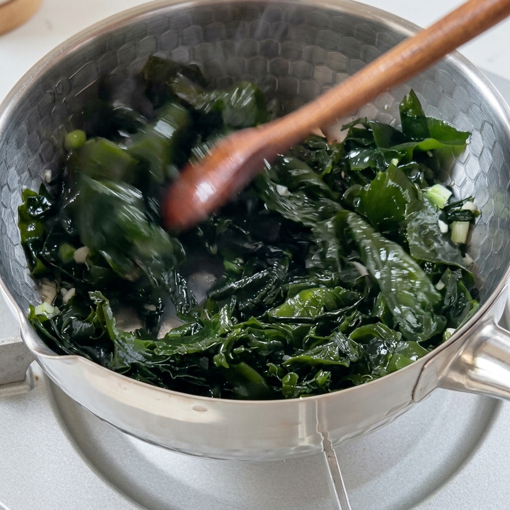 Algues wakame vertes réhydratées mélangées avec des aromates dans une marmite en métal.