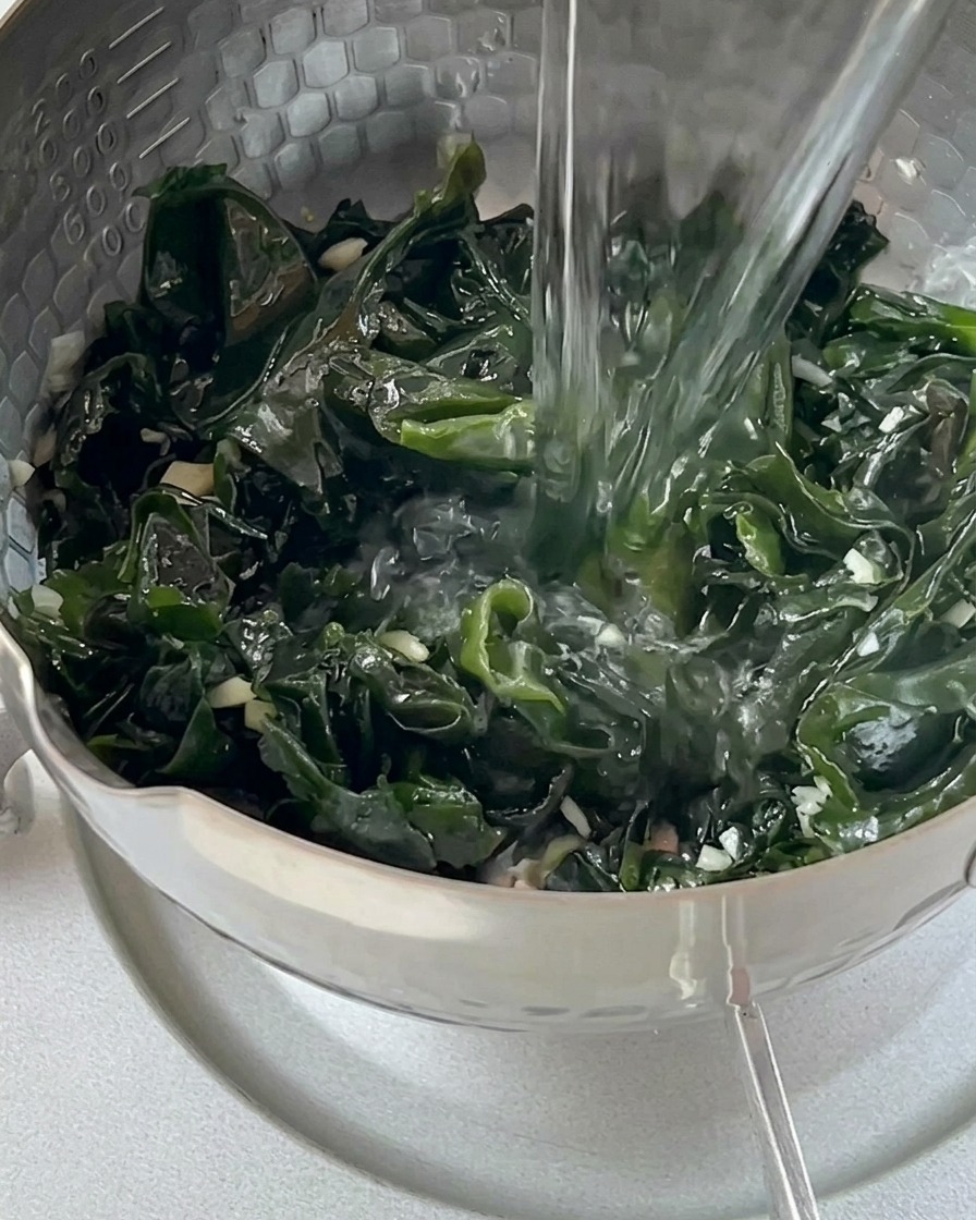 Leau bouillante dune bouilloire en verre est versée sur le wakame vert dans une marmite.